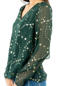 Långärmad grön blus med V-ringning, featuring en genomskinlig textur och spridda guldstjärnmönster. Lämplig för avslappnad användning.