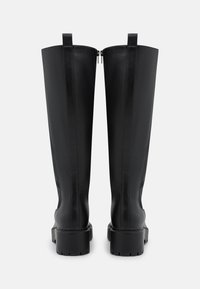 Schwarze kniehohe Stiefel aus glattem Leder, ausgestattet mit robustem Blockabsatz und Reißverschluss. Strukturierte Oberfläche mit Ziehschlaufen oben.