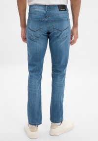 Jeans en denim bleu clair avec une coupe slim, dotés de deux poches arrière avec des surpiqûres décoratives et d'un petit patch logo sur la ceinture.