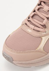 Scarpa sportiva di un rosa chiaro con tomaia in rete, suola ammortizzata e punta rinforzata. Presenta cuciture tonali e un dettaglio di branding discreto.