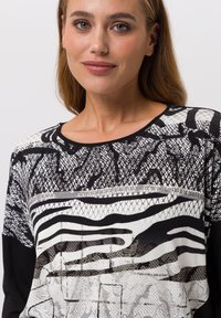 Schwarz-weißes Langarmoberteil mit einer Mischung aus geometrischen und Tiermustern, runder Halsauschnitt und strukturiertem Stoff.