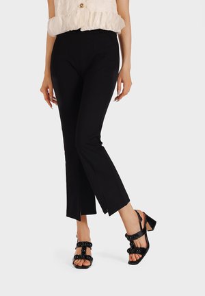 Pantaloni neri a cropped con vestibilità slim e dettaglio a spacco all'orlo, abbinati a décolleté neri con cinturino alla caviglia caratterizzati da accentuazioni rotonde.