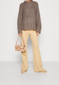 Maglione marrone chunky lavorato a maglia con collo arrotolato, abbinato a pantaloni palazzo beige e scarpe con platform beige chiaro. Borsa bianca con accessori dorati.