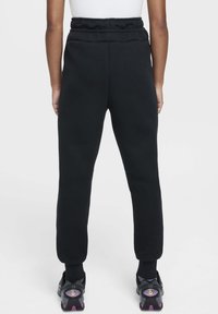 Pantalon de survêtement en coton noir avec taille à cordon, jambes fuselées et côtes au bas. Associé à des chaussures de sport noires et roses.