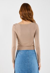 Ljusbrun långärmad topp med rundad halsringning, åtsittande design och mjukt material, kombinerad med en blå denimkjol med en slits.