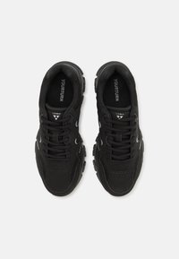 Des baskets de sport noires avec un mélange de matériaux texturés, des panneaux en mesh, un design à lacets et des semelles extérieures en caoutchouc proéminentes avec des accents.
