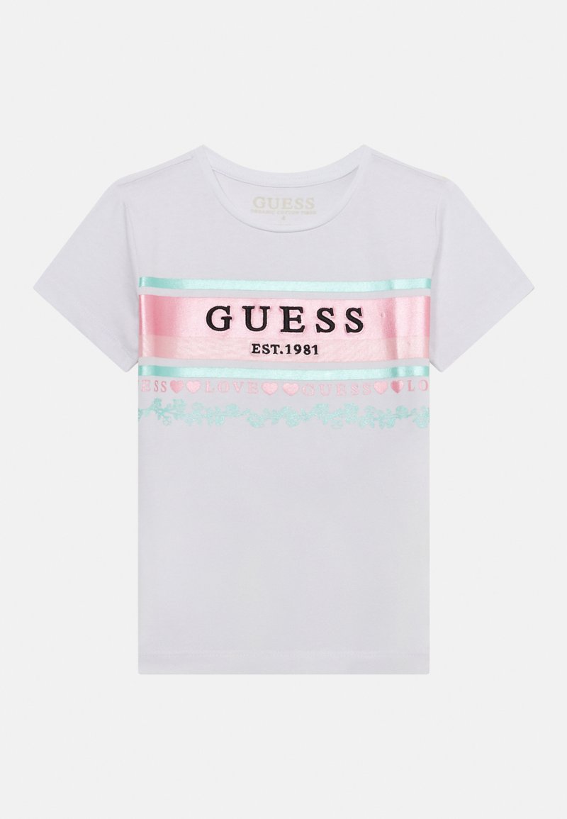 Bela kratka majica s kratkimi rokavi, ki vsebuje obarvane vodoravne črte in črn napis "GUESS EST.1981" z dekorativnimi motivi v pastelnih barvah.