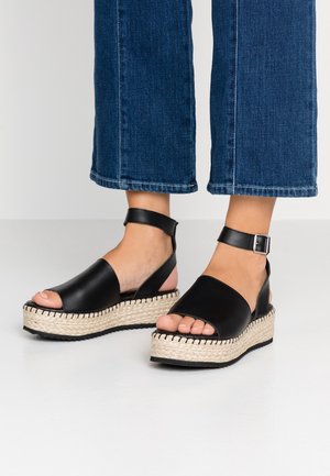 Czarne skórzane espadryle na płaskiej podeszwie z otwartym noskiem, z plecioną jucie platformą oraz paskiem wokół kostki z detalem z klamrą.