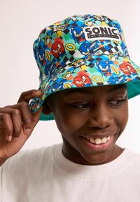Bucket-Hut mit einem bunten Sonic the Hedgehog-Print, der Charaktere und Ringe zeigt, aus einem Stoff mit glatter Textur.