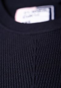 Tessuto a coste di un maglione blu scuro con scollatura rotonda e un motivo testurizzato sottile. L'etichetta è visibile sul colletto con le istruzioni per la cura.