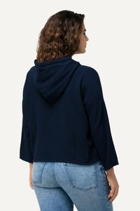 Navyblaue Kapuzenjacke aus strukturiertem Stoff und mit verkürztem Design. Mit weiten Ärmeln und lässiger Passform, kombiniert mit hellblauen Jeans.