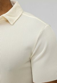 Polo shirt couleur crème avec un design en ribette texturé et un col classique. Les manches ajustées mettent en valeur la silhouette élancée du polo.
