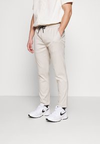 Beige randiga byxor med ett elastiskt midjeband och svart dragsko, i kombination med vita Nike-sneakers. Slät tyg med en skräddarsydd passform.