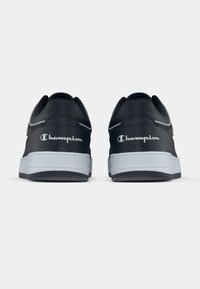 Czarne trampki z gładkim wierzchem, białą gumową podeszwą i wypukłym logo „Champion” na pięcie. Zaokrąglony nosek z kontrastowym przeszyciem.