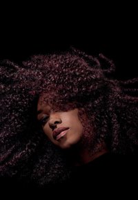 Dunkles, voluminöses Haar mit definierten Locken und einem tiefen Burgunderrot-Stich. Der Hintergrund ist schwarz, wodurch das Haar und die Gesichtszüge hervorgehoben werden.