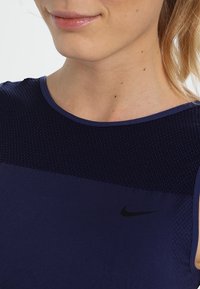 Námořnická modrá sportovní tílko s texturovanou horní částí, hladkou spodní částí a černým logem Nike na hrudi.