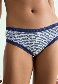 Painetut bikinihousut, joissa on tummansininen pitsireunus. Kangas on valkoisen ja tummansinisen abstraktin kuvion pehmeästi teksturoima.