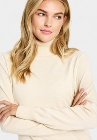 Bēšs turtlenecks džemperis ar ribota tipa apkakli un aprocēm, izgatavots no mīksta materiāla, ar pieguļošu dizainu un gludu tekstūru.