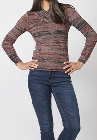 Haut à manches longues et col en V, présentant une texture en maille chinée rouge, noire et grise. Comprend un détail décoratif avec une fermeture éclair au niveau de l'encolure.