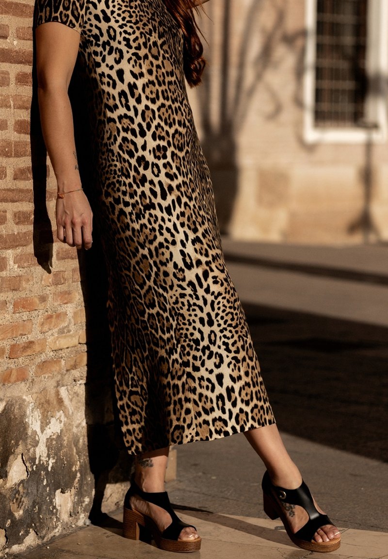 Vestido midi de estampado de leopardo con mangas cortas, que presenta un diseño fluido. Sandalias de plataforma negras con acentos recortados y tacones de madera.