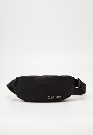 Sort Calvin Klein bæltetaske med lynlåslukning og justerbar rem, vist på hvid baggrund.