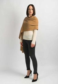 Brun cashmere sjal svøbt om en lys sweater, parret med tætsiddende sorte jeans og sorte højhælede sko. Glatte, lagdelte teksturer.