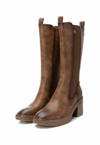 Botas marrones hasta la rodilla con una parte superior de cuero liso, paneles laterales elásticos y un tacón de bloque texturizado. Detalle de costura notable en la suela.