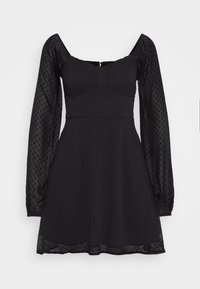 Svart klänning med en figursydd överdel, fyrkantig halsringning och långa genomskinliga puffärmar med prickig textur. Utsvängd kjol med fodrad fåll.