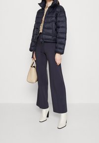 Námořnicky modrá péřová bunda s vysokým límcem a elastickým šňůrkovým stahováním, doplněná širokými námořnicky modrými kalhotami a bílými botami na podpatku. Akcent v podobě béžové kabelky.