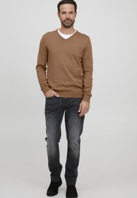Rjav pulover s V-izrezom in gladko teksturo, v kombinaciji z sivo jeans hlačami. Oblačilo vključuje črne gležnjarje. Preprost dizajn z minimalnimi detajli.