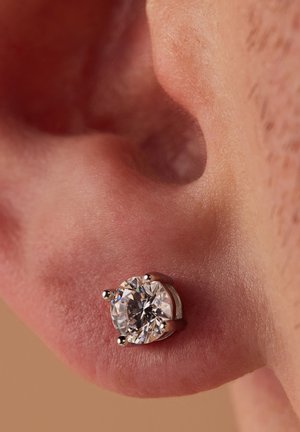 Round diamond stud earring in a metal setting, featuring four prongs to secure the stone, closely positioned to the earlobe.