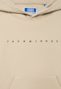 Μπεζ φούτερ με μεγάλη τσέπη και κουκούλα με κορδόνι. Διαθέτει μαύρο κείμενο "JACK & JONES" τυπωμένο μπροστά. Μαλακή υφή υφάσματος.