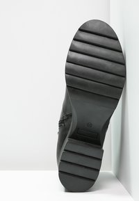 Bota de cuero negro con una suela de goma texturizada, que presenta ranuras horizontales para mayor tracción y un ligero estrechamiento hacia la punta.