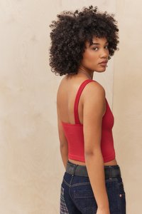 Top corto a righe rosso con spalline sottili, abbinato a jeans blu con accenti texture, su uno sfondo di legno chiaro.