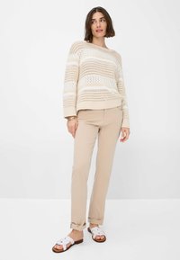 Beige gebreide trui met open weefsel, voorzien van horizontale witte strepen. Gecombineerd met lichtbeige broeken en witte sandalen met een bloemenpatroon.