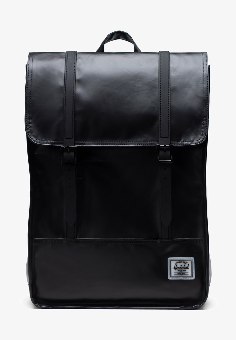 Mochila negra con un acabado brillante, que cuenta con correas ajustables, un cierre de solapa y un bolsillo frontal con un parche de logo.