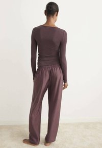 Top ajustado de manga larga en burdeos oscuro combinado con pantalones sueltos de pierna ancha del mismo color; ambas prendas tienen un acabado suave y texturizado.