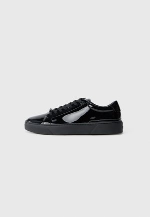 Czarne sneakersy z lakierowanej skóry o gładkiej fakturze, grubej czarnej gumowej podeszwie, okrągłym nosku i czarnych sznurowadłach; minimalistyczny design bez wzorów.