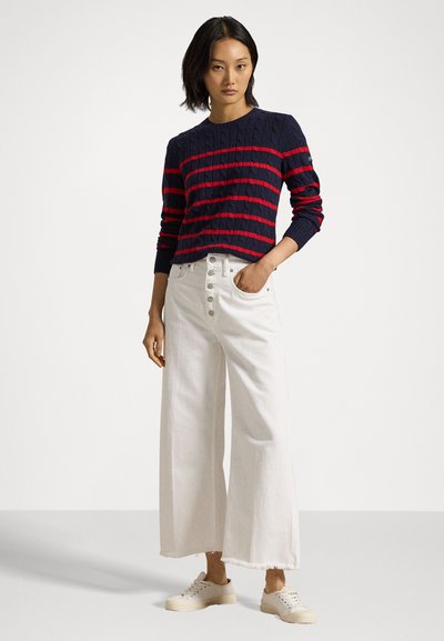 Pull en maille cablée rayé rouge et marine avec un col rond, associé à un pantalon large blanc agrémenté de boutons sur le devant et d'ourlets effilochés.