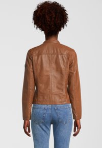 Braune Lederjacke mit einer taillierten Passform, die einen hohen Kragen und gestickte Details aufweist. Kombiniert mit blauen Jeans.