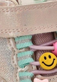 Zapatillas de color rosa claro con acentos metálicos, tela texturizada, cordones elásticos coloridos con charms en forma de cara sonriente y corazón.