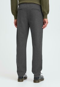Szare dresowe spodnie z teksturowanej tkaniny, elastycznym pasem i dwoma skośnymi tylnymi kieszeniami. Połączone z czarnymi butami i widocznymi detalami wykończenia.