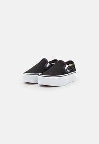 Black canvas slip-on shoes with a white rubber sole, featuring contrasting white stitching and a rounded toe design.