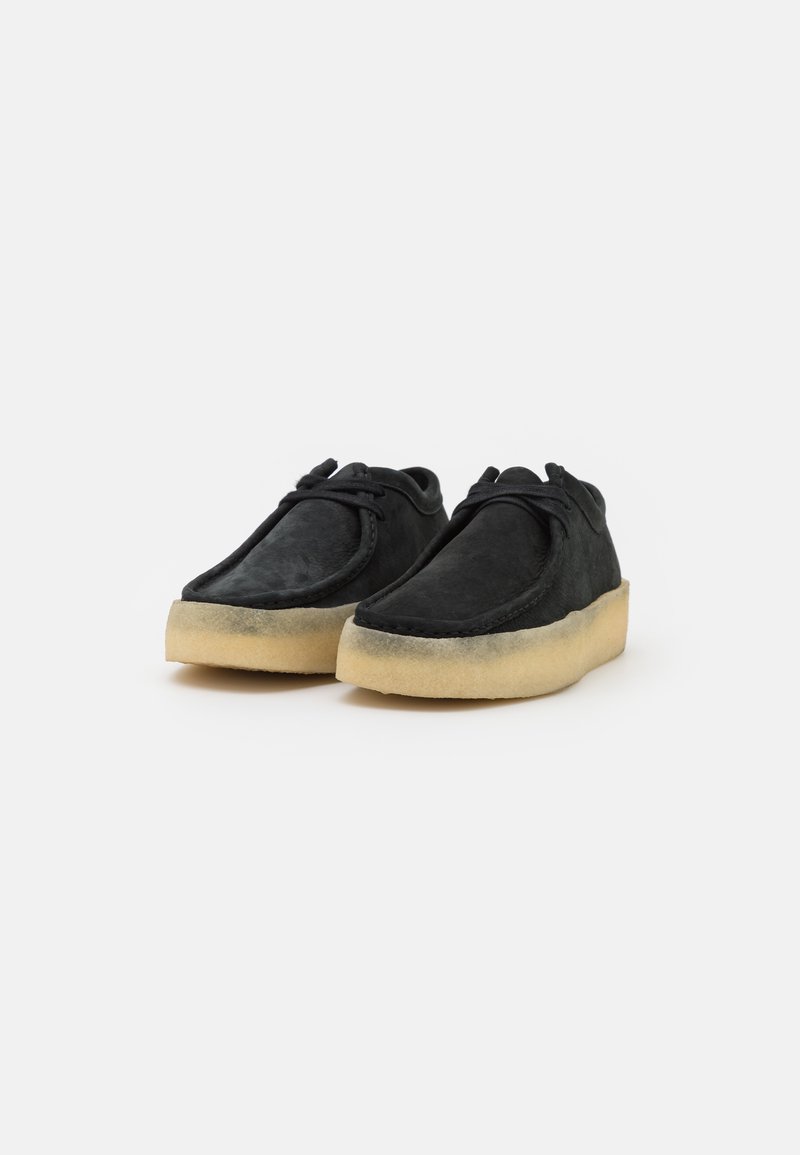 Scarpe in suede nere con punta rotonda, caratterizzate da una suola in gomma chiara e un laccio davanti. Il design è semplice e minimale.