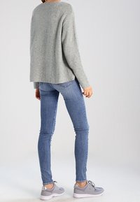 Jersey de punto azul claro, jeans ajustados azules y zapatillas grises con suelas blancas. El jersey tiene un corte relajado y una textura suave.