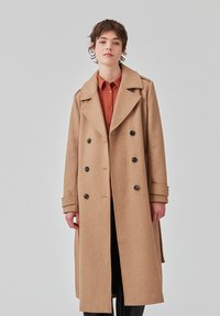 Cappotto in lana color cammello con design doppiopetto, ampi colletti e bottoni neri. Presenta una vestibilità su misura e maniche lunghe.