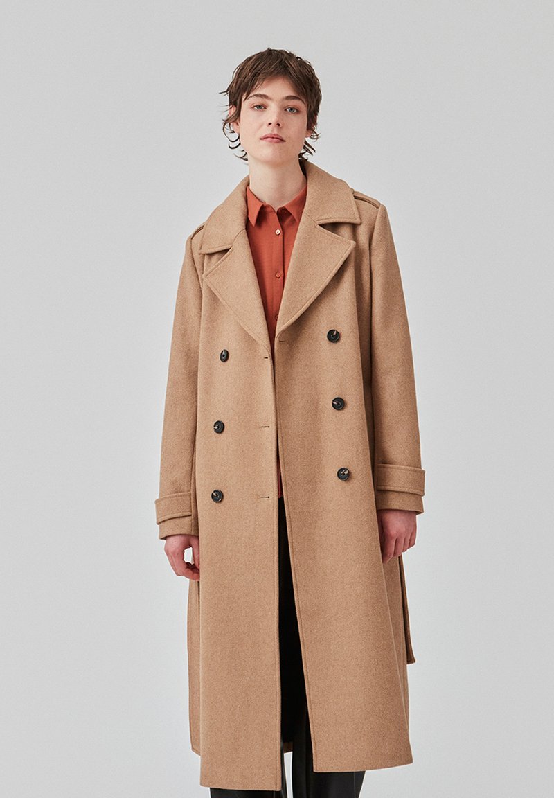 Cappotto in lana color cammello con design doppiopetto, ampi colletti e bottoni neri. Presenta una vestibilità su misura e maniche lunghe.