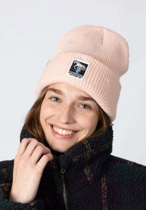 Vaaleanpunainen neulepipo, jossa on käännetty reunus ja värikäs paikka. Mallilla on yllään musta fleecetakki, jossa on vetoketju.