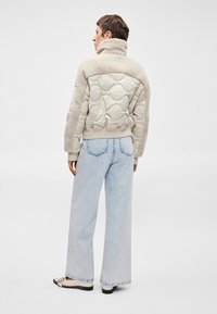 Beige steppelt dzseki puha, szőrmére hasonlító gallérral és vállrészekkel, világoskék bő derekú farmernadrággal és krémszínű cipőkkel párosítva.