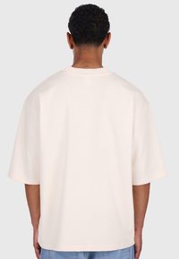 Lys pink oversized t-shirt med korte ærmer, blød tekstur, rund hals og lige kant, båret med blå denimjeans.